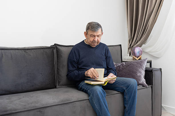 istock Elderly man reading book on sofa at home 2252694299