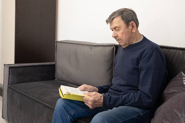 istock Elderly man reading book on sofa at home 2252694375