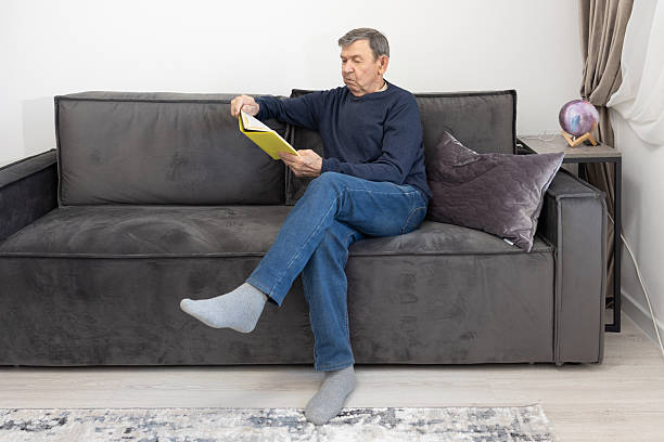 istock Elderly man reading book on sofa at home 2252694906