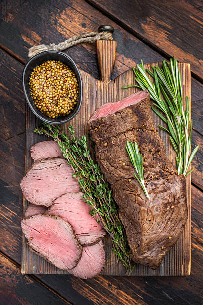 Classic roast beef medium rare with thyme rosemary and spices on rustic board dark background overhead food photo