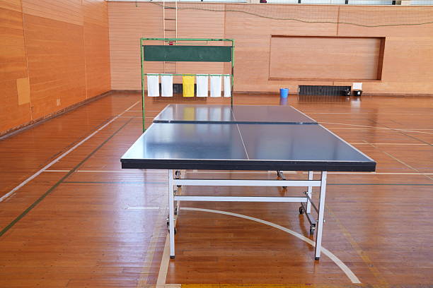 A ping pong table sits in a gymnasium. The table is empty and the floor is wooden
