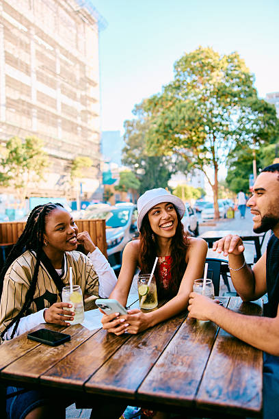 Relaxed group of friends laughing together while enjoying drinks at an outdoor cafe table in the city