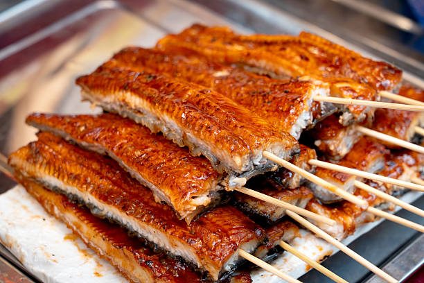 Glossy, caramelized Japanese grilled unagi (eel) skewers stacked at a traditional street food market.