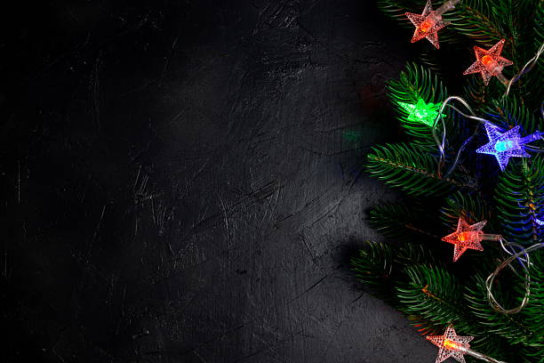 Colorful star lights shine on pine branches, creating a festive decoration suitable for holiday celebrations. The background shows a dark, textured surface enhancing the visuals.