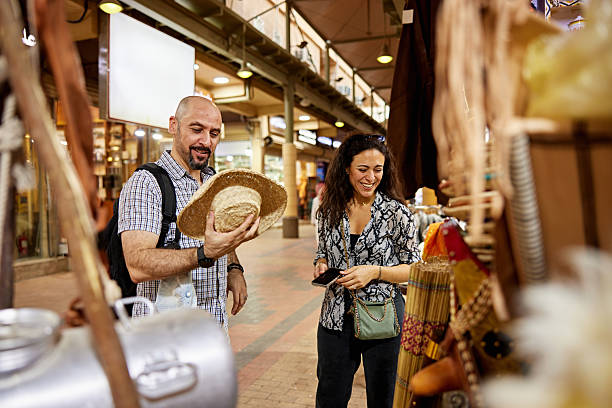 Man and woman in 30s and 40s examining hats and other craft products at traditional marketplace.