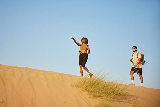 istock Adventurers exploring desert dunes, woman pointing distant view 2252725740