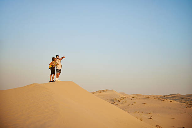 istock Couple exploring desert sand dune pointing to horizon 2252725765