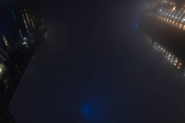 Abstract urban photography of light patterns from building windows blurred by heavy nighttime haze. Foggy night cityscape with illuminated office building windows glowing through dense mist.