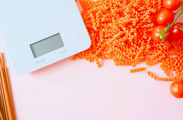 Minimal flat lay featuring whole-grain pasta and cherry tomatoes beside a digital kitchen scale on a soft pastel background. The image represents New Year’s resolutions, portion control, and illness prevention through mindful nutrition. Large copy space makes it ideal for health, medical, and dietary campaigns.