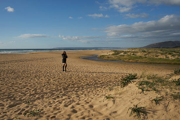 Woman standing on a quiet sandy beach with a small stream, ocean, and dunes