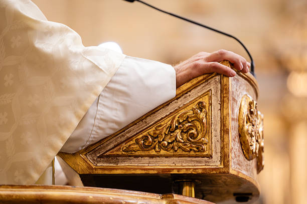 Priest's hand gently resting on an antique golden pulpit with intricate carvings, delivering a sermon during a religious ceremony inside a church with warm lighting