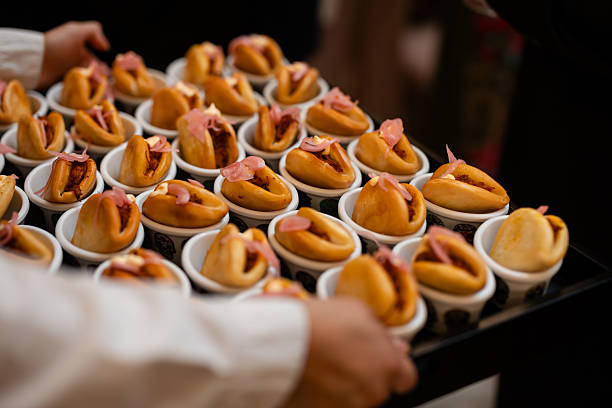 Server presents trays of steamed bao buns filled with savory ingredients and pickled onions, arranged as gourmet finger-food for weddings, receptions, and catered events