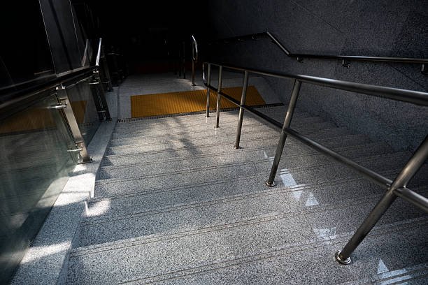 A staircase with metal handrails leading down to a yellow step. The scene is dimly lit, creating a moody atmosphere. Potential use for architectural or safety-related content.