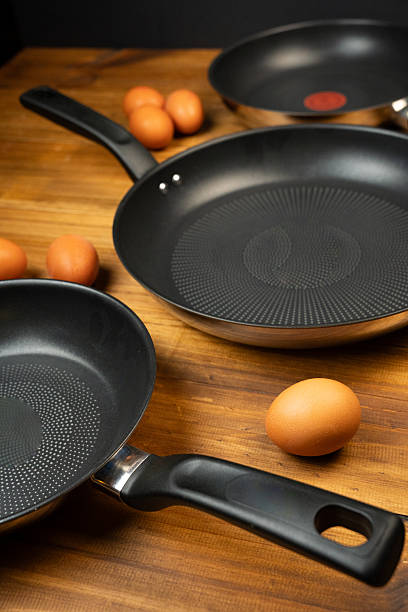 istock Kitchen scene with multiple non-stick frying pans and fresh brown eggs on a rustic wooden table 2252744383