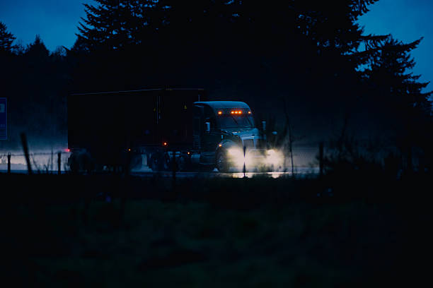Semi-Truck with trailer on the freeway in the rain, at dusk. Headlights are on, and conditions are questionable.