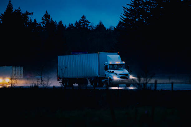 Semi-Truck with trailer on the freeway in the rain, at dusk. Headlights are on, and conditions are questionable.