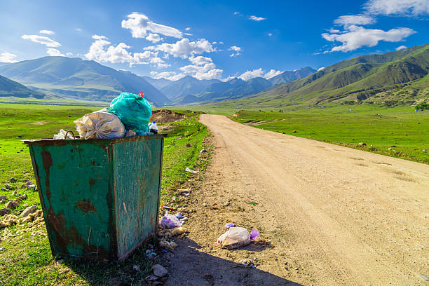 Overflowing trash can filled with bags and loose garbage reflects environmental concern. Scattered trash around highlights pollution and neglect in scenic nature.