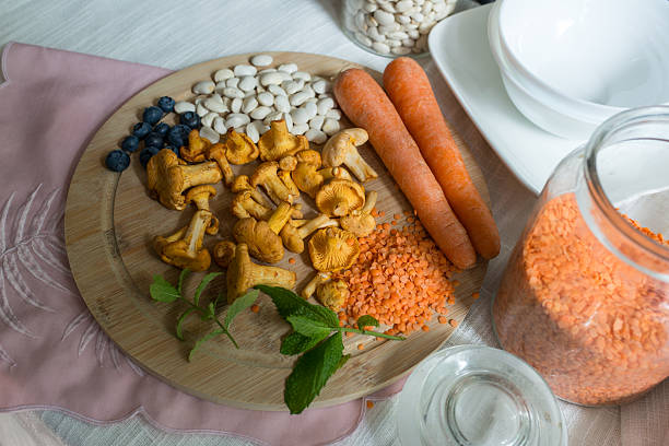 Overhead composition of cooking ingredients on a wooden board: chanterelle mushrooms, red lentils, white beans, carrots, blueberries, and mint beside jars and bowls. Clean meal prep concept for healthy recipe, pantry staples, and home cooking.
