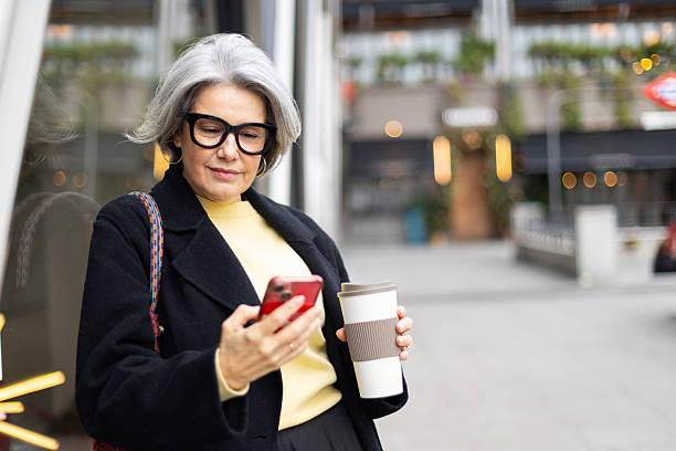 istock Senior woman using smartphone and drinking coffee in city 2252757900