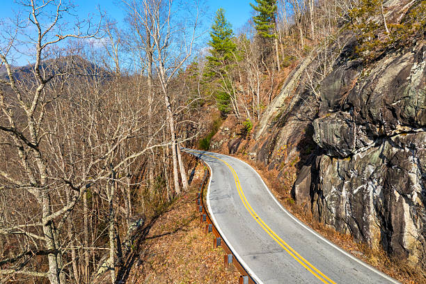 Scenic parkway road winds through rugged mountain terrain. Steep hillside and autumn forest surround driving on Highlands Road, North Carolina.