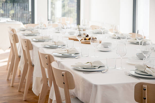 istock A bright elegant dining hall is prepared for a festive gathering, with a long white table neatly set with plates, glasses and linen napkins, ready to welcome guests for a celebratory meal. 2252760933