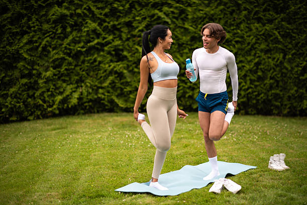 Young couple stretching their legs together on a yoga mat in a green park.