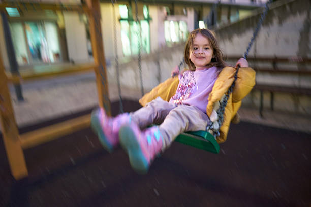 Young girl enjoying fun on a playground swing at night.