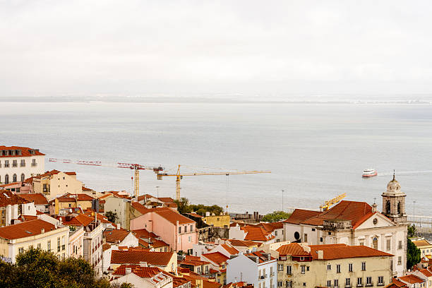 Lisbon Portugal December 05 2025. A wide cityscape shows Alfama rooftops descending toward the Tagus River.