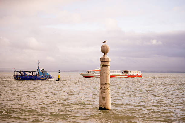 Lisbon Portugal December 05 2025. Tourist boats pass a stone river navigation marker on the Tagus River during daylight.