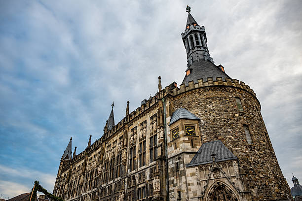 Low angle view of a historic Gothic town hall facade and stone tower under dramatic winter clouds, ideal for travel, heritage and architecture use.