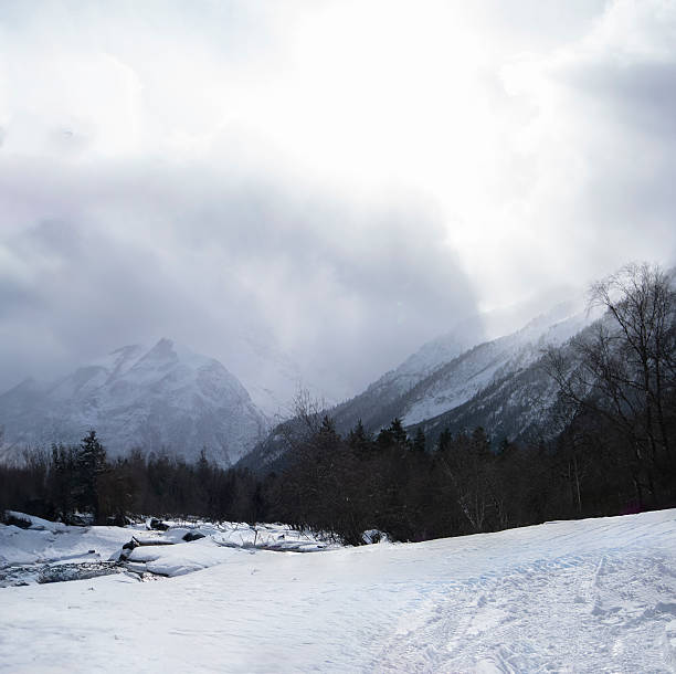 Snow-covered ground and towering mountains are visible under a cloudy sky.