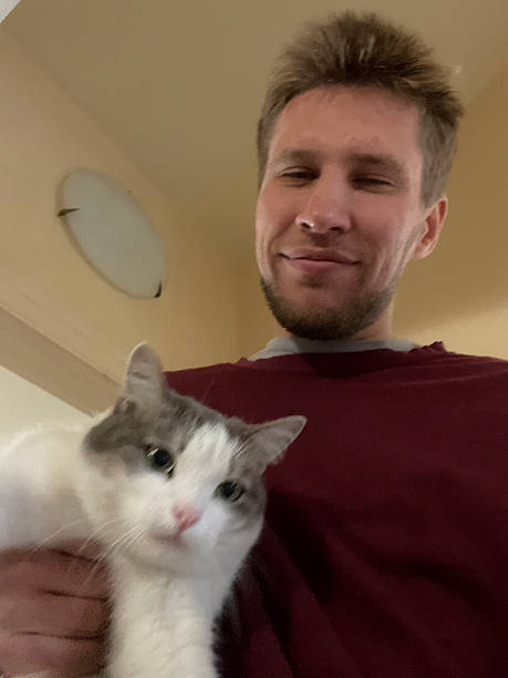 istock Man smiles while holding a gray and white cat in a warm indoor setting 2252782536