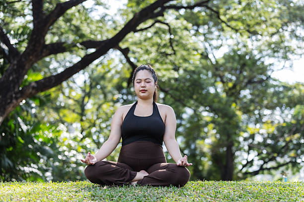 istock A calm plus-size Asian woman sits cross-legged in meditation on green grass, practicing mindfulness and balance. A peaceful outdoor wellness scene that promotes body positivity, mental health, and inner strength. 2252791413
