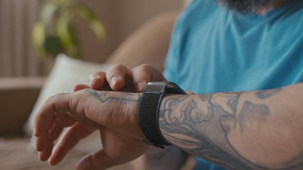 Man relaxing on his living room sofa while using his computer and looking at his smartwatch