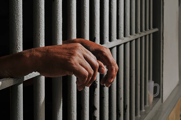 istock hands of a prisoner behind prison bars on black background 2252806761
