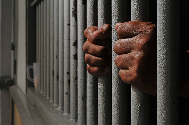 istock hands of a prisoner behind prison bars on black background 2252806777