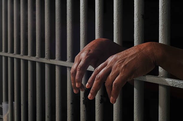 istock hands of a prisoner behind prison bars on black background 2252806780