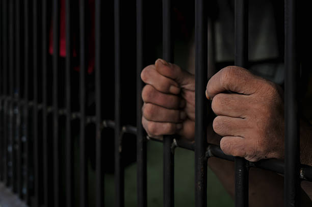 istock hands of a prisoner behind prison bars on black background 2252806800