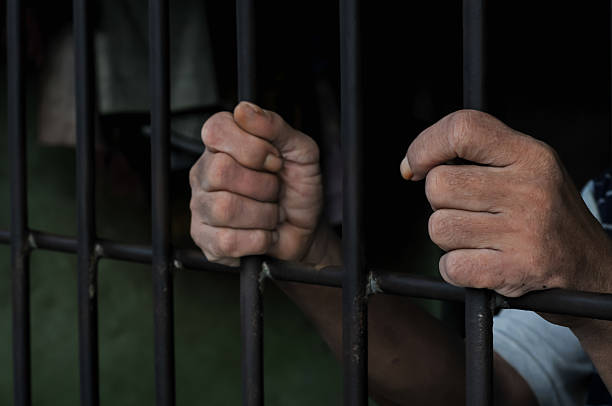 istock hands of a prisoner behind prison bars on black background 2252806805