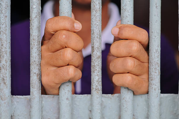 istock hands of a prisoner behind prison bars on black background 2252806825
