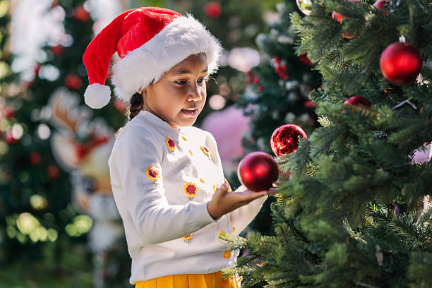 istock A joyful child wearing a Santa hat decorates a Christmas tree outdoors, surrounded by festive lights and ornaments. The scene captures holiday spirit, childhood happiness, family traditions, and seasonal celebration. 2252809522