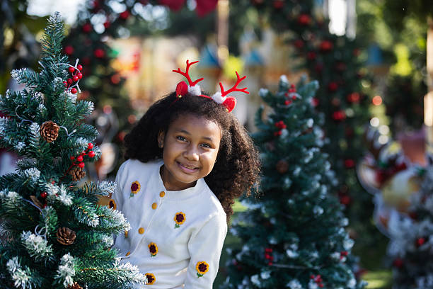 istock A cheerful child wearing reindeer antlers waves hello while standing among decorated Christmas trees. The scene reflects festive warmth, holiday joy, childhood innocence, and seasonal celebration in an outdoor setting. 2252809532