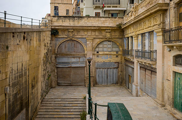 A view of the historic architecture in Valletta, Malta. The image shows closed shops and the Grand Harbour Hotel, capturing the city's unique blend of history and urban life.