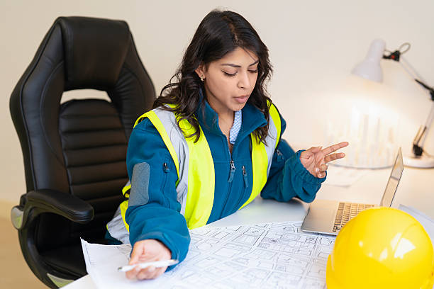 istock Female Professional builder engineer discussing building plans while seated at desk in office 2252811694