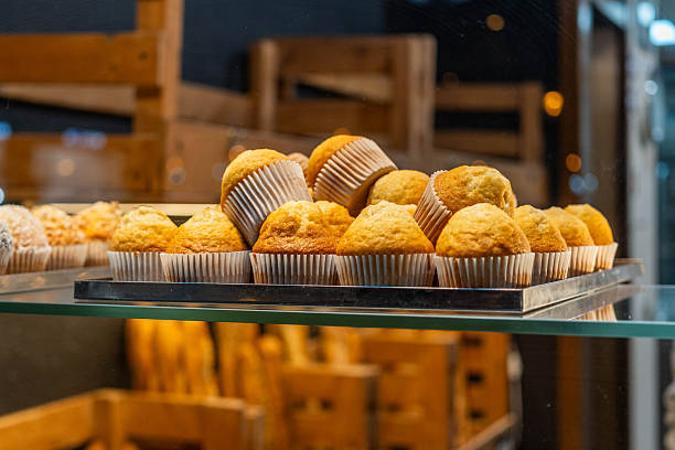 A display of freshly baked muffins arranged on a tray, showcasing a variety of golden-brown muffins with paper liners, set in a bakery environment