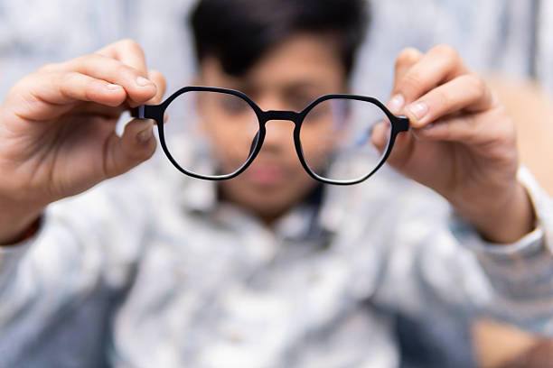 Portrait of Indian little boy checking eye glasses before wearing them. Eye Sight Problem Concept.