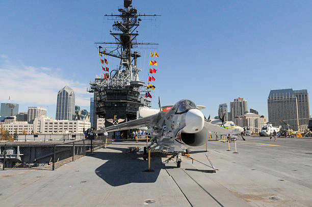 A large aircraft carrier docked at sunset with planes on deck reflecting in calm waters.
