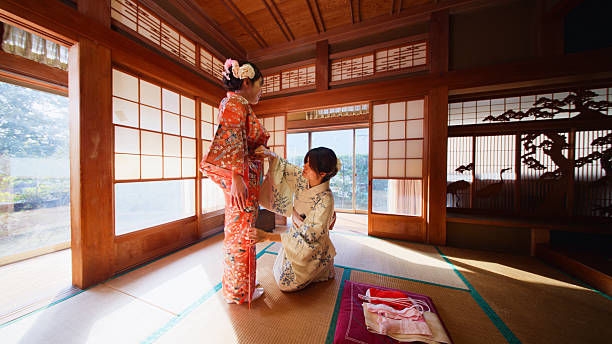 A woman is getting dressed and applied make-up by a professional in a traditional Japanese room, washitsu.