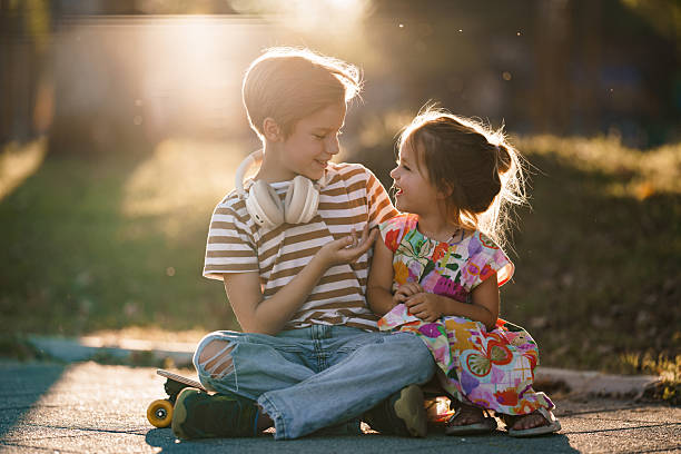 Young brother and sister bonding with affection, sitting on a skateboard in nature.