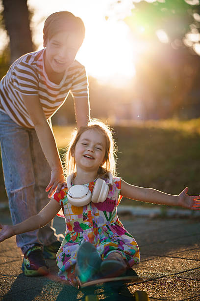 istock Brother helping sister learning skateboarding at sunset. 2252822491